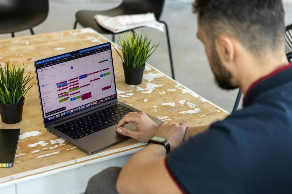 Man working remotely at a desk with a laptop open to a calendar app.