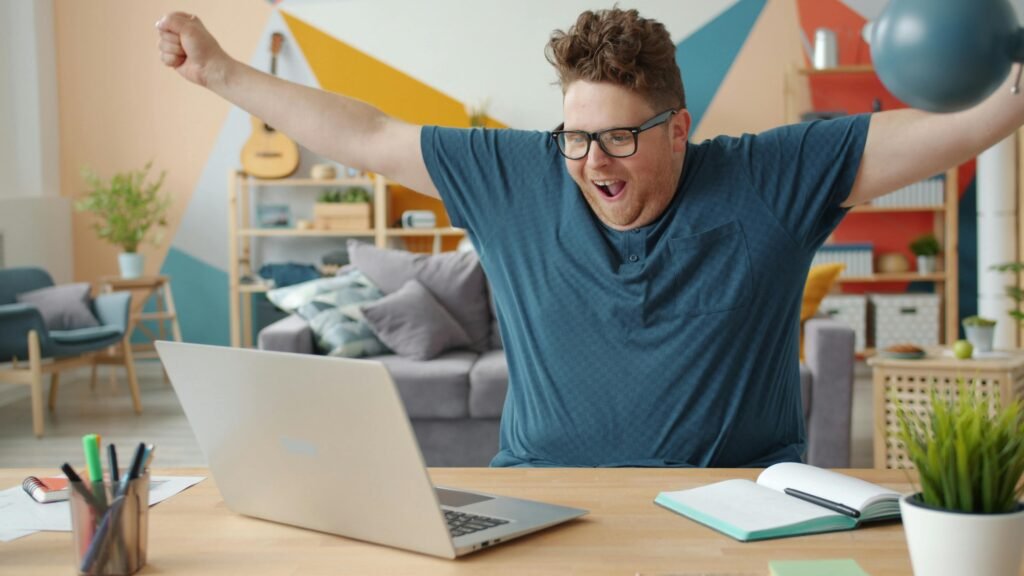 Joyful man celebrating success at home office, arms raised in excitement.