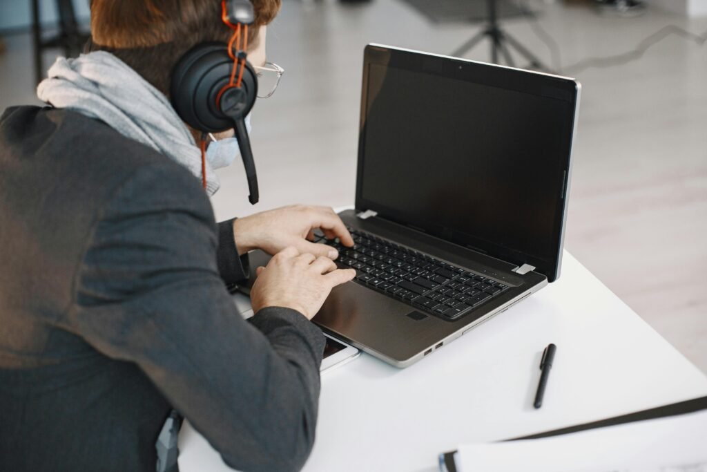 Focused man wearing headphones using a laptop for remote work in a modern office setting.
