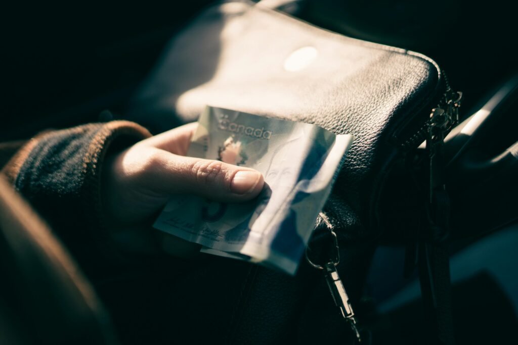 A person holding a Canadian five-dollar bill close to a leather handbag, showcasing financial transactions.