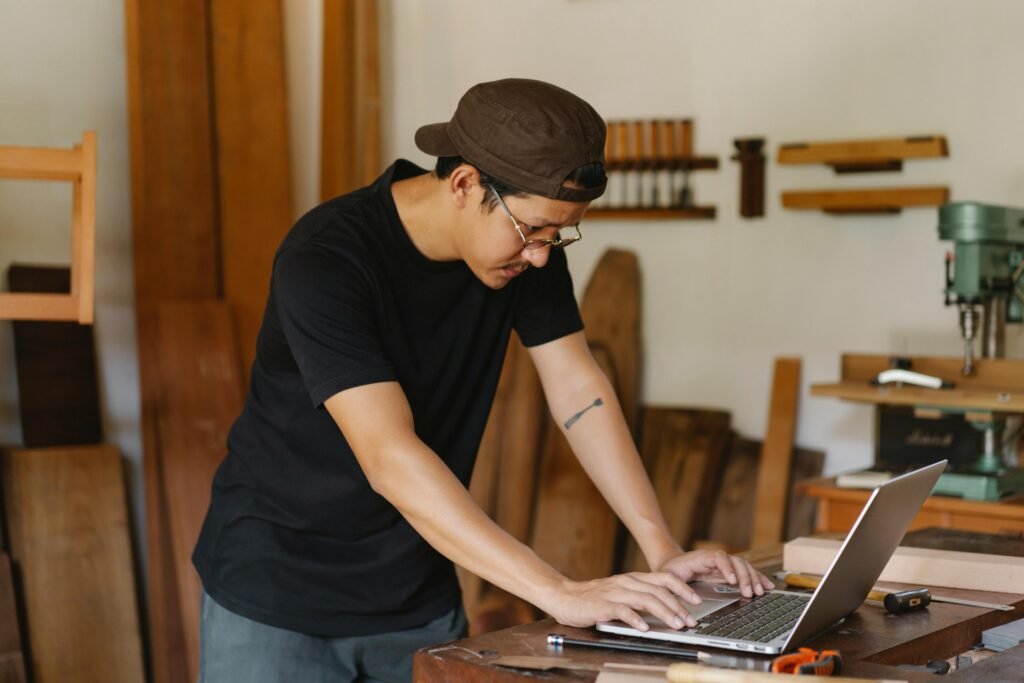 Concentrated ethnic man in casual clothes and eyeglasses browsing netbook while working in creative workspace in daytime
