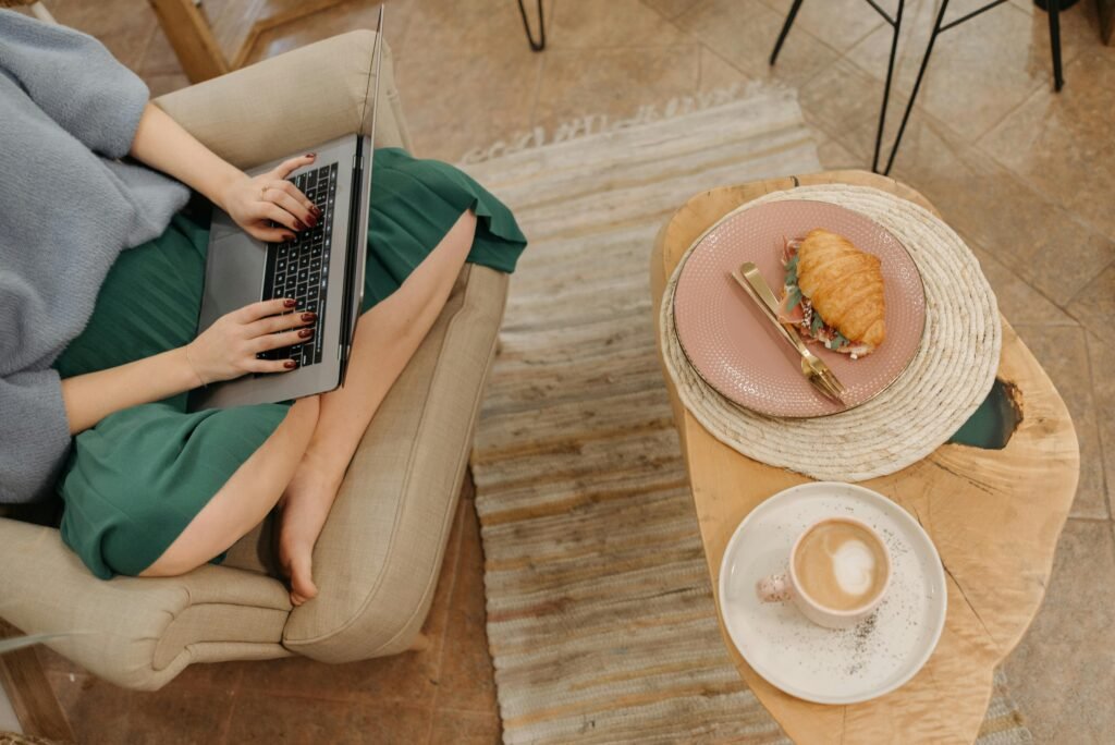 Woman working comfortably on a laptop with coffee and croissant in a cozy home setting.