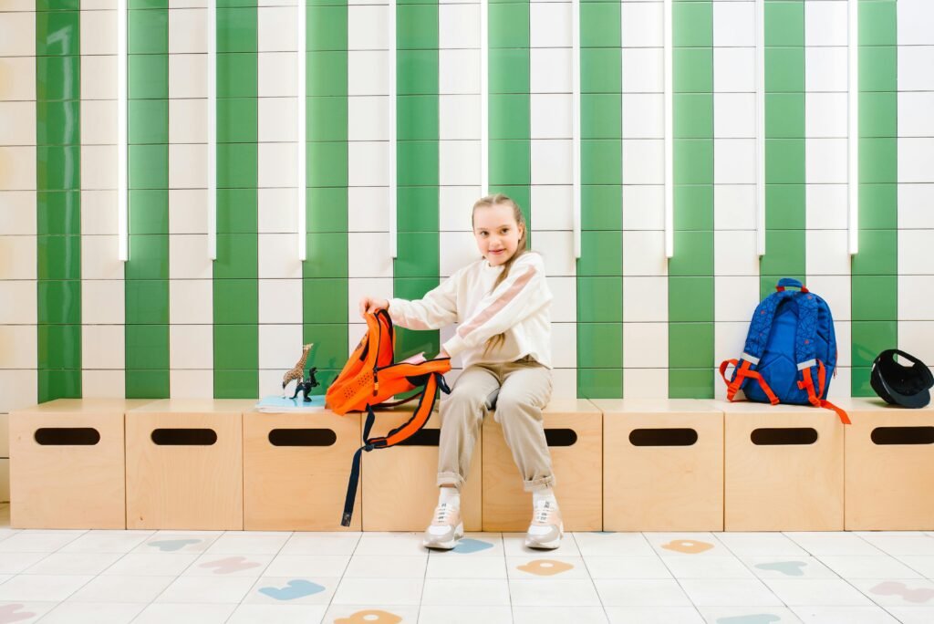 A young girl smiles while packing her backpack in a school locker room with bright decor.